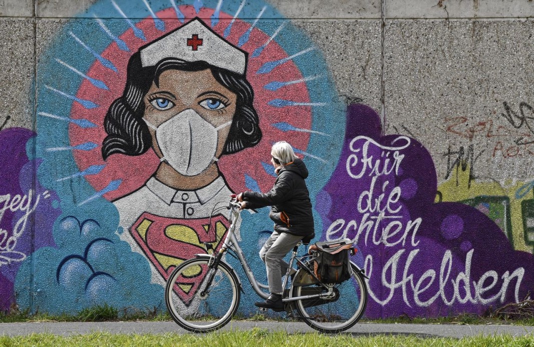 Жена на велосипед минава покрай графит в германския град Хам, изобразяващ Супер жена с послание до нея „за истинските герои“. Снимка БТА