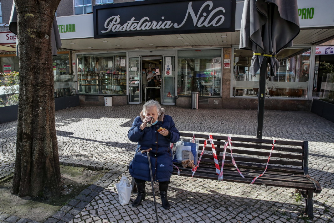 Възрастна жена пие кафе и яде кифла пред сладкарница след повторното отваряне на „несъществени“ търговски обекти и фризьорски салони, Лисабон, Португалия, 15 март 2021 г. През миналия месец португалското правителство започна да облекчава ограниченията и блокирането, наложени в средата на януари заради Covid-19. Правителството разреши възобновяването на работата на детските градини, училища, фризьорски салони и библиотеки от 15 март.