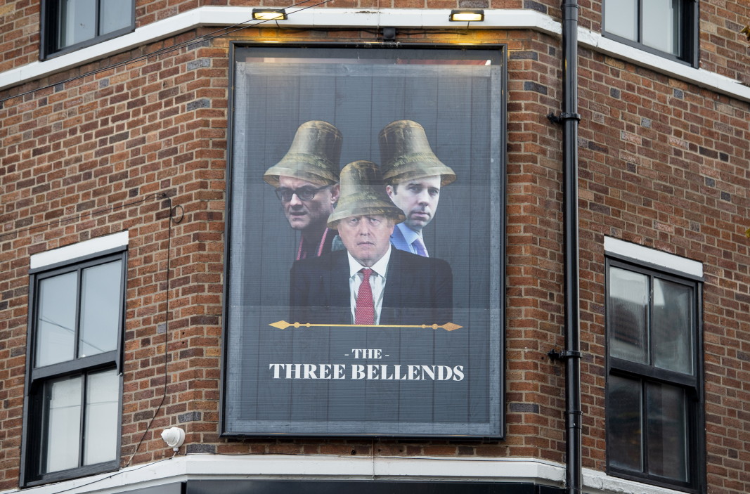 Изображение на министър-председателя на Великобритания Борис Джонсън, здравния министър Мат Ханкок и специалния съветник Доминик Къмингс на табела пред заведение, преименувано на The Three Bellends (Трите разклонения) в знак на протест срещу правителственото отношение към пандемията от коронавирус, Ню Брайтън, Уирал, Англия - октомври 2020 г.