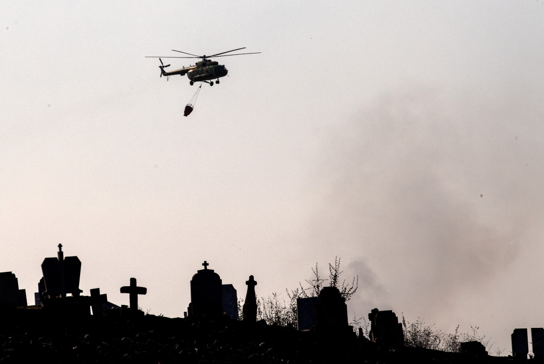 Противопожарен хеликоптер лети над гробище близо до района, засегнат от горски пожари до село Неманджици, близо до Свети Николе, Северна Македония, 30 юли 2024 г.; ЕПА/БГНЕС
