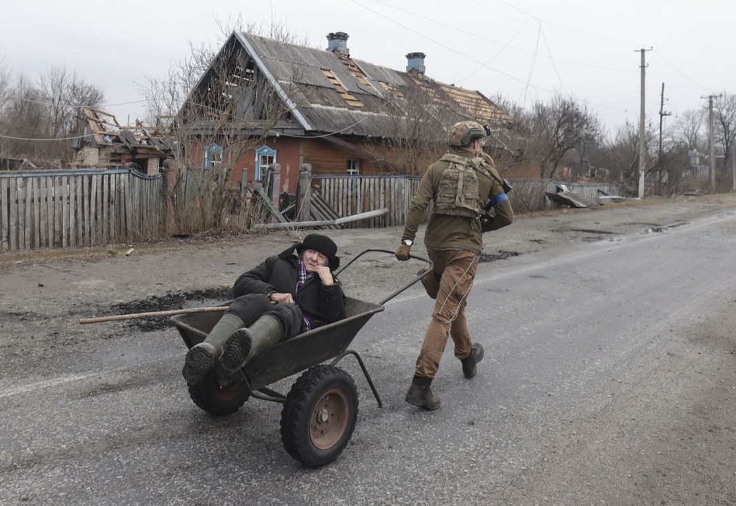 Украински военнослужещ евакуира възрастен мъж от повредената му къща в село Тетерив край Киев, 31 март 2022 г. Снимка: ЕПА/БГНЕС