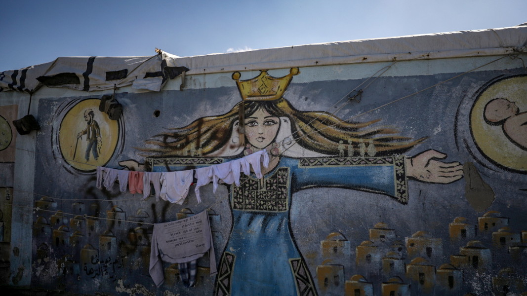 Детски дрехи на разселени палестинци съхнат, закачени на фона на графити върху училищна стена в южната част на Ивицата Газа, март 2024 г. Снимка: ЕПА/БГНЕС