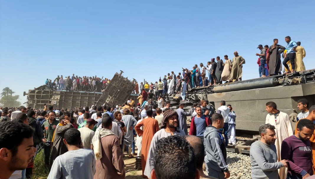 Хора са се качили върху преобърнат вагон и на близка постройка на мястото на влакова катастрофа в провинция Сохаг, Египет, 26 март 2021 г.
