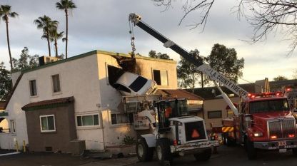 Специален кран на пожарната се опитва да освободи забилата се кола във втория етаж на сграда в Санта Ана, Калифорния.