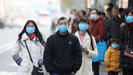 Китайци с маски чакат автобус до затворения рибен пазар Хуанан в град Ухан, провинция Хубей, смятан, че е свързан с появата на новия вирус.