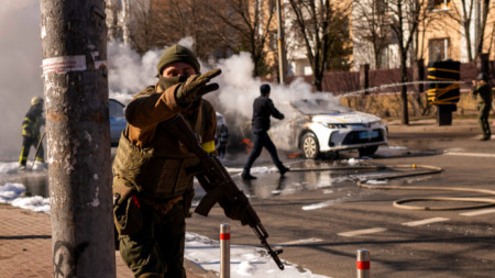 Украински войници заемат позиции пред военен обект в Киев, докато коли горят край тях, 26 февруари 2022 г.