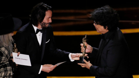 Авторът на „Паразит“ Пон Джун Хо приема наградата за оригинален сценарий от Киану Рийвс. 