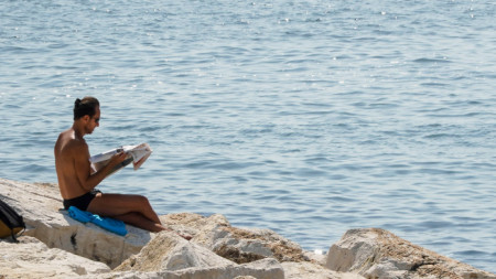 Снимката е илюстративна - любител на слънцето и морето чете вестник край Неапол.