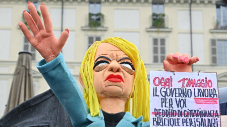 Марионетка, изобразяваща италианската премиерка Мелони, държи плакат с надпис 