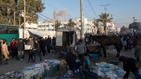 Разселени палестинци в бежанския лагер Хан Юнис, на фона на дим след израелски удар, южната част на Ивицата Газа, 19 декември 2023 г. 