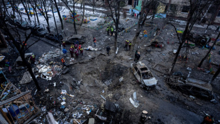 Хора стоят около кратер в двора на мноогоежтажна жилищна сграда в Киев след руска бомбардировка. 