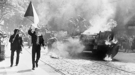 Чехословаци носят националното знаме покрай горящ съветски танк в Прага.