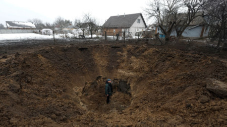 :Мъж стои в кратер, причинен от удар на руска ракета, в село Копилив край Киев, 14 януари 2023 г.