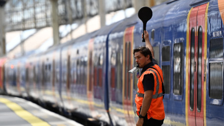 Служител на Network Rail сигнализира за един от малкото влакове, заминаващи от гара Ватерло в Лондон, 21 юни 2022 г.