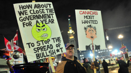 Протестиращ канадец с плакати е застанал близо до парламента, докато и шофьорите на камиони продължават да протестират срещу мандатите за ваксинация, Отава, Канада, 8 февруари 2022 г.