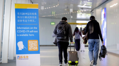 Пътници от Китай преминават до надпис с информация за безплатно тестване за Covid-19 на летище 