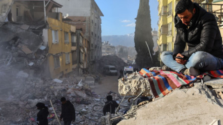 Мъж седи сред развалините в Хатай, Турция, 15 февруари 2023 г.