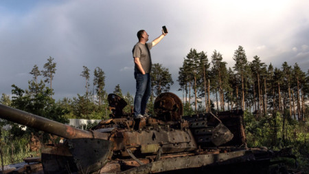 Мъж си прави селфи върху разрушена бронирана машина близо до Ирпин, Киевска област, 22 юни 2022 г.