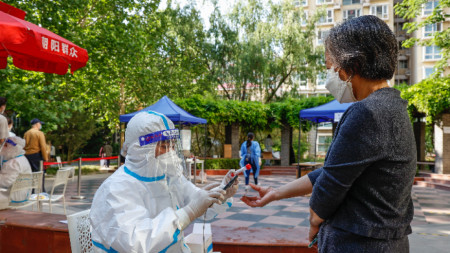 Пекин продължава масовите Covid тестове, на снимката: Служител в защитен костюм  прави снимка на личната карта на жена и тестване, Пекин, Китай, 16 май 2022 г. 