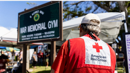 Служител на Американския Червен кръст на входа на стадиона War Memorial, превърнат в подслон за жителите на Лахайна след пожар, който унищожи града, Хавай, САЩ, 12 август 2023 г.