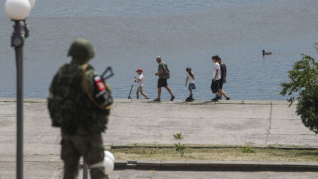 Хора се разхождат край река Днепър в Херсон под погледа на руски военен, 20 май 2022 г.