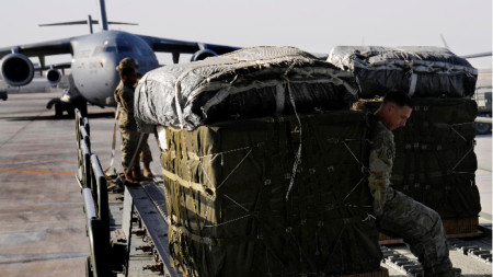 Американски военнослужещ от Военновъздушните сили на САЩ товари контейнери с хуманитарна помощ на транспортен самолет в базата 