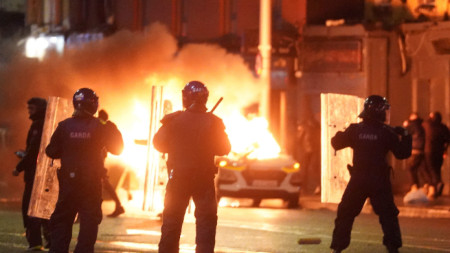 Ирландски полицаи край кола, обхваната от пламъци, на мястото на днешното нападение с нож в Дъблин - 23 ноември 2023 г.