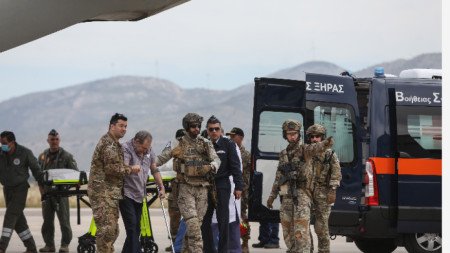 Военен персонал помага на група гръцки граждани, евакуирани от Судан, докато слизат от военен самолет C-27 Spartan на военното летище 