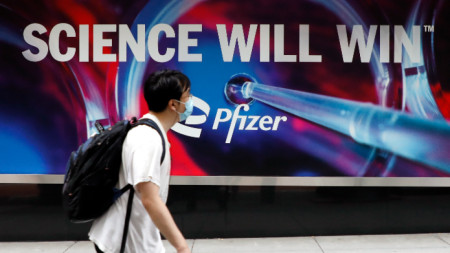 Мъж с маска минава покрай табела пред централата на фармацевтичната компания Pfizer в Ню Йорк.