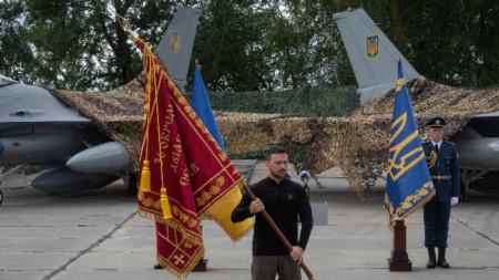 Володимир Зеленски връчва знамето на военна част по случай Деня на ВВС на фона на изтребителите Ф-16 на неразкрито място в Украйна, 4 август 2024 г.