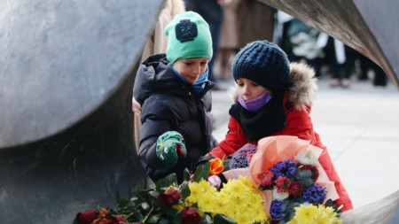 Деца поднасят цветя на Паметника на спасението в градинката на Софийския университет