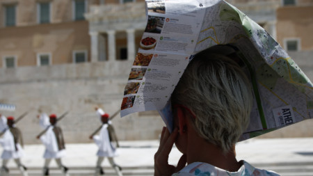 Жена покрива главата си с туристически флаер, за да се предпази от слънцето, докато наблюдава гръцката президентска гвардия  в центъра на Атина, август 2021 г.