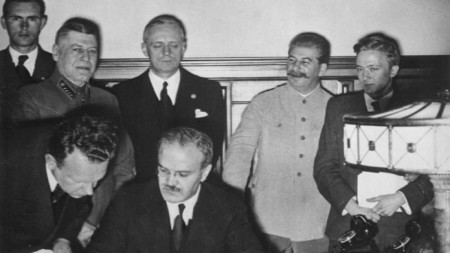 Вячеслав Молотов подписва пакта за ненападение между Германия и СССР. На заден план в средата: Йоахим фон Рибентроп и Йосиф Сталин.