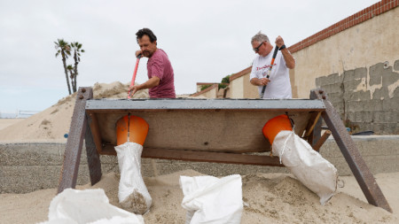 Майк Евънс (вляво) и Томи Гудуин (вдясно) пълнят торби с пясък, с които укрепват домовете си в Сийл Бийч, Калифорния, САЩ, 19 август 2023 г.