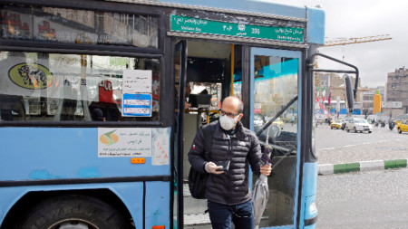 Жител на Техеран със защитна маска слиза от автобус на градския транспорт в иранската столица