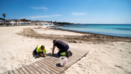 Работници подготвят плаж на испанския остров Менорка в очакване на решение за отварянето му за посетители.